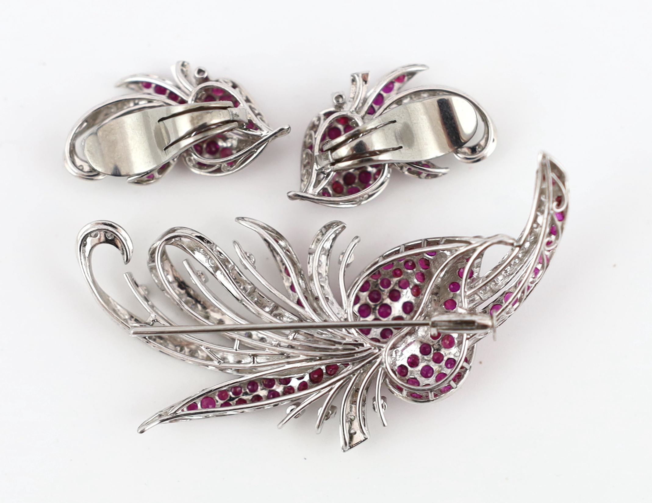 A suite of platinum?, diamond and ruby set cluster jewellery, comprising a spray brooch and pair of matching ear clips